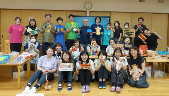 研修参加者がおのおのに玩具を手に持ち、講師を囲んで撮影した集合写真