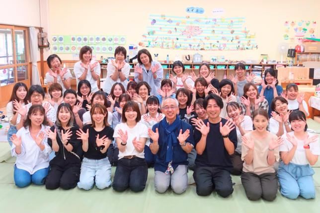 日本知育玩具協会の保育士向け研修に参加した講師と保育士たちの集合写真。研修室で全員が笑顔で両手を上げ、和やかな雰囲気で記念撮影