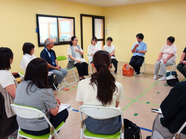 保育の実践を学ぶ見学会の一場面。3園の園長・職員が輪になって座り、見学した園の取り組みについて感想や気づきを語り合っている