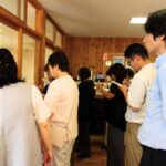 保育室を外がら見学する参加者たちの様子。棚に並ぶ商品を見ながら、メモを取ったり説明に耳を傾けたりしている後ろ姿