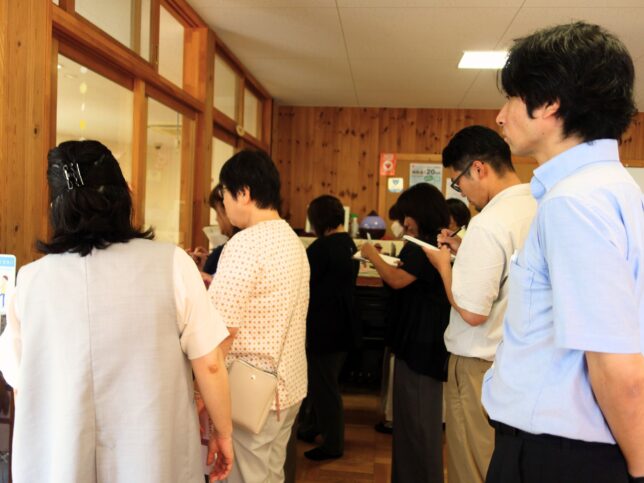 保育室を外がら見学する参加者たちの様子。棚に並ぶ商品を見ながら、メモを取ったり説明に耳を傾けたりしている後ろ姿