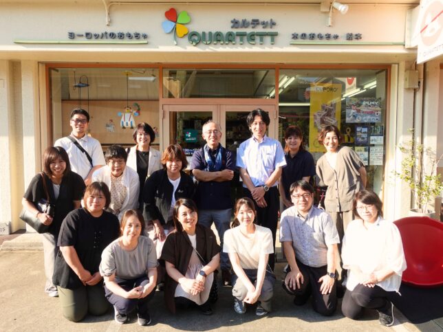 おもちゃと絵本の専門店カルテット店舗前で撮影した集合写真。見学会の参加者たちが店の入り口前に並び、笑顔で記念撮影している