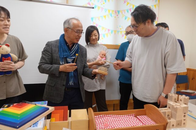 木のおもちゃを使った園内研修の一場面。講師が実際のおもちゃを手に、遊び方や発達への効果を保育士たちに実演しながら伝えている