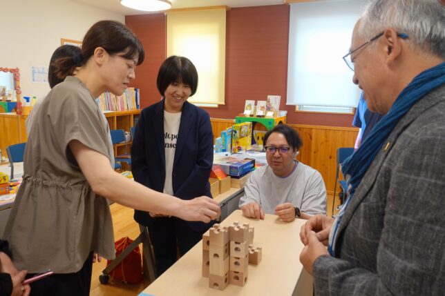「おもちゃと子どもの発達」研修の実践パート。園長先生方が木製積木を手に取り、実際に組み立てながらその魅力を体感している様子